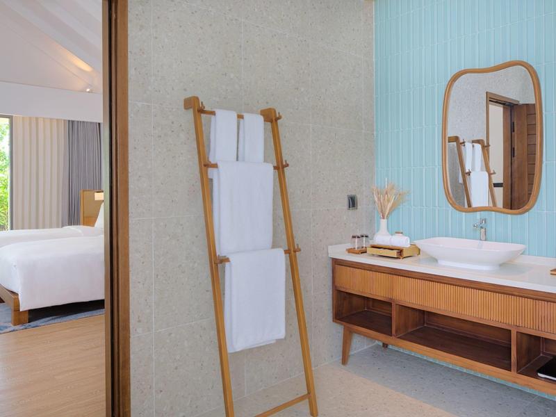 Salle de bain avec échelle en bois contre le mur, serviettes et vue sur la chambre avec grand lit.