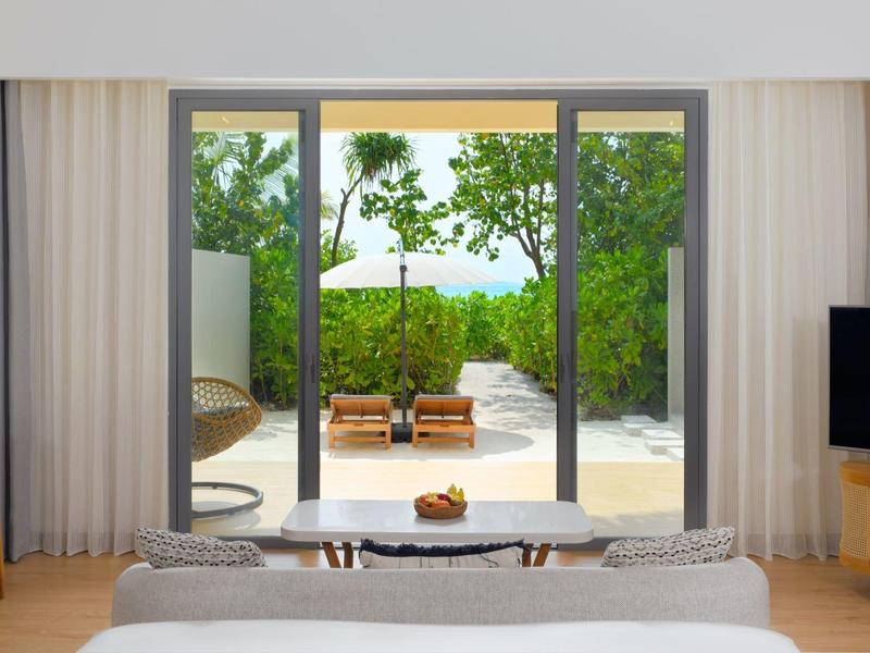 Chambre d'hôtel moderne avec lit double, balcon et vue sur deux transats dans le jardin.