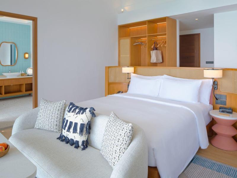 Chambre d'hôtel moderne avec grand lit, canapé, accents en bois, décor lumineux et accueillant.