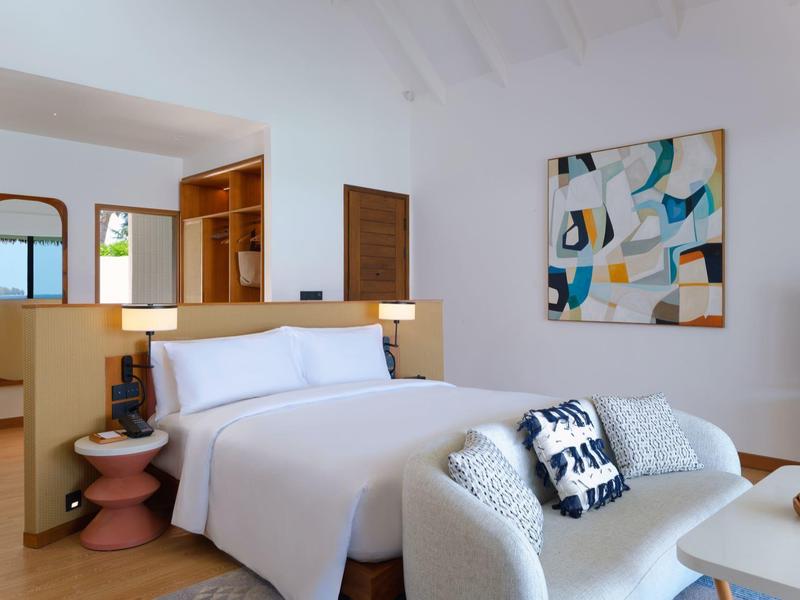 Chambre d'hôtel lumineuse avec lit double, canapé, œuvre d'art moderne et meubles en bois.