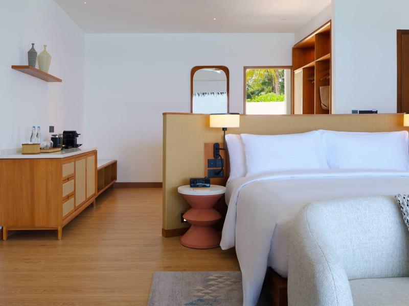 Chambre moderne et lumineuse avec lit double, tables de chevet et commode avec objets décoratifs.