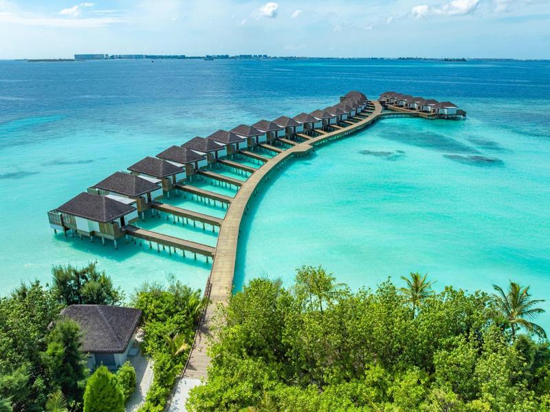 Bungalows sur pilotis s'étendant en courbe sur une eau turquoise claire.