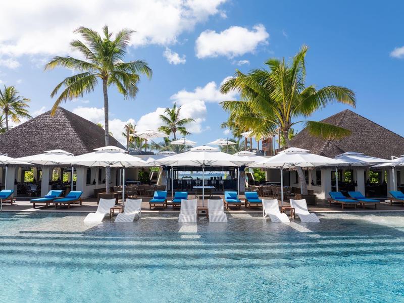 Piscine avec chaises longues et parasols devant des bungalows tropicaux sous un ciel bleu