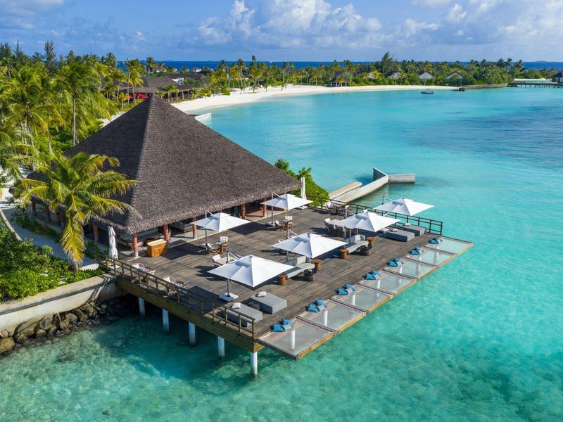 Complexe de luxe avec terrasse ensoleillée et chaises longues au-dessus de l'eau turquoise claire.