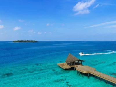 Molo in legno con capanna dal tetto di paglia su acqua turchese trasparente e cielo soleggiato.