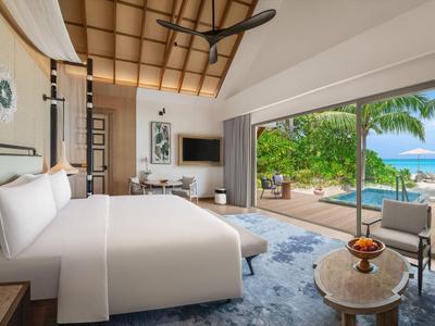 Moderne hotelkamer met groot bed, tapijt en uitzicht op tropische tuin en zee.