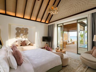 Helles Schlafzimmer mit Dachschräge, gemütlichem Bett und Zugang zu Terrasse mit Sitzbereich.