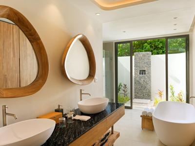 Modernes Badezimmer mit zwei ovalen Spiegeln, Waschbecken, freistehender Badewanne und Blick ins Grüne.