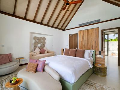 Heller, moderner Hotelzimmer mit hohen Decken, großem Bett, Holzschränken und Sitzbereich.