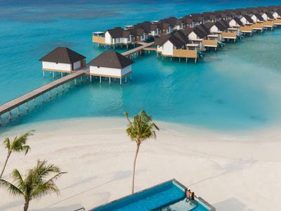 Überwasserbungalows mit Reihenbungalows an türkisblauem Wasser und weißem Sandstrand mit Pool.