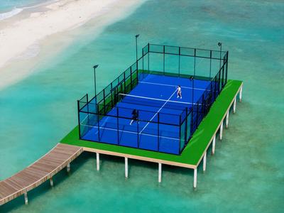 Padel-Tennisplatz auf einer Plattform im türkisfarbenen Meer neben einem Holzsteg.