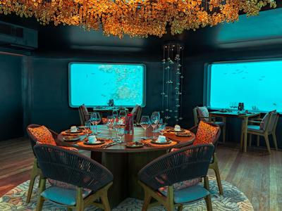 Unterwasser-Restaurant mit rundem Tisch und großem Fenster mit Meeresblick.