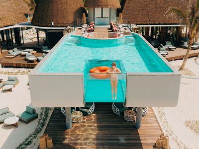 Schwimmbad mit Infinity-Design und Sonnendeck vor spitzen Dächern in einem Resort.