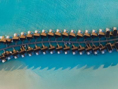 Reihen von Wasserbungalows über türkisfarbenem Wasser an einem tropischen Strand.