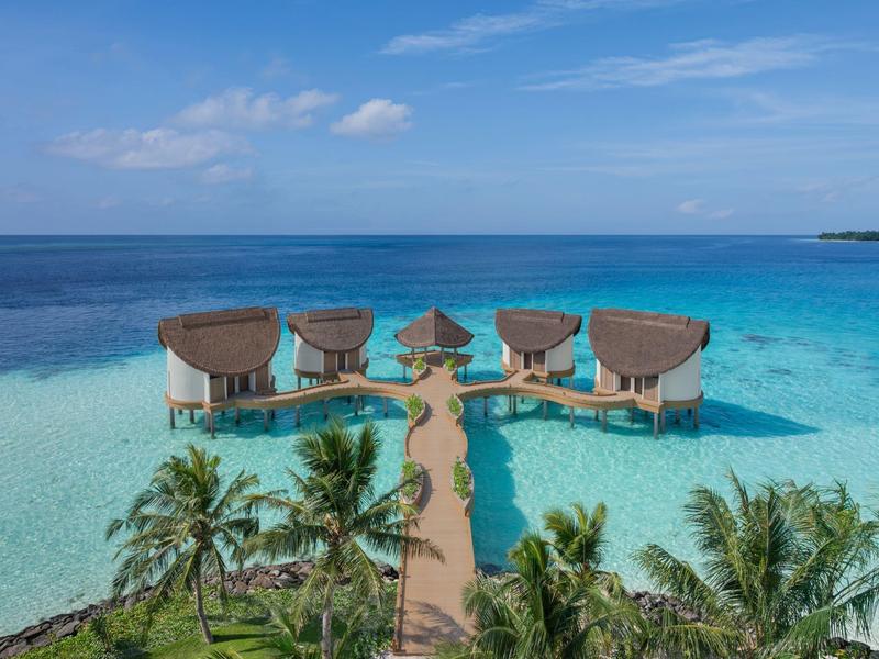 Bungalow su palafitte su acque turchesi limpide con palme e cielo azzurro.