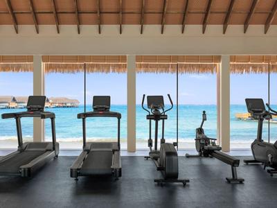 Gimnasio moderno con vista al mar a través de grandes ventanas, equipado con cintas de correr y bicicletas.