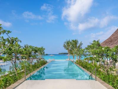 Blick auf einen infinity Pool mit Blick auf das Meer und umgeben von grüner Vegetation und Himmel.