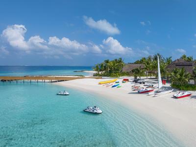 Playa de arena blanca con barcos coloridos y agua azul clara cerca de un resort tropical.