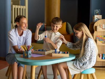 Drei Personen sitzen um einen runden Tisch und spielen mit bunten Stäbchen in einem gemütlichen Raum.
