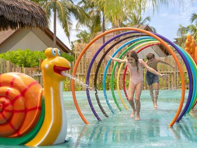 Kinder spielen in einem Wasserpark mit bunten Bögen und einer Schneckenskulptur.