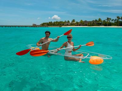 Dos personas remando en un kayak transparente sobre agua turquesa clara cerca de una isla.