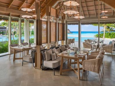 Offenes Restaurant mit Tischen und Stühlen, Blick auf tropische Außenanlage und Meer