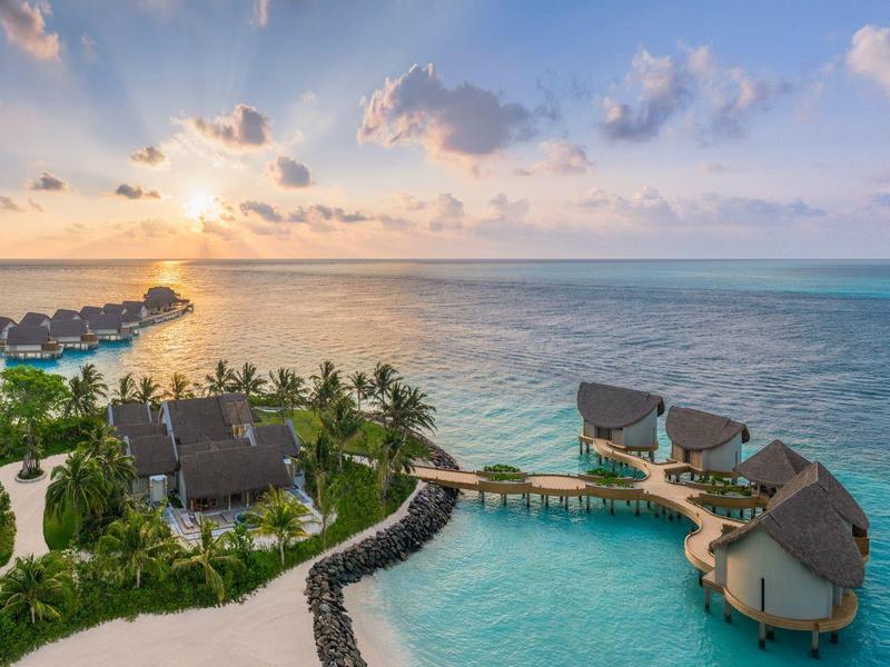 Luxuriöse Wasserbungalows und Pool bei Sonnenuntergang am tropischen Strand.