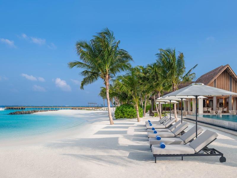 Strand mit Liegestühlen, Palmen und einem Resort-Gebäude unter blauem Himmel