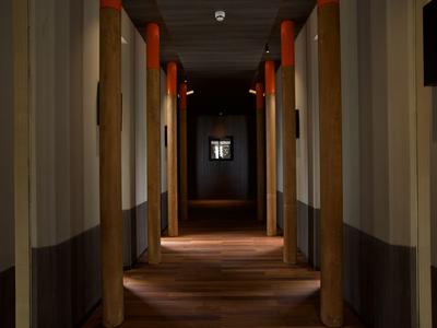 Flur eines Hotels mit Holzboden und mehreren Türen, warm beleuchtet und schmal.