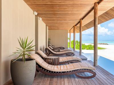 Moderne Liegestühle aus Holz mit Kissen stehen auf einer Holzterrasse neben einem Pool mit Blick auf den Strand.