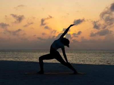 Person praktiziert Yoga am Strand während des Sonnenuntergangs mit ruhigem Meer im Hintergrund.