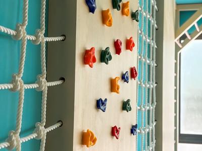 Kletterwand mit bunten Griffen und Sicherheitsnetz in einem hellen, modernen Innenraum.