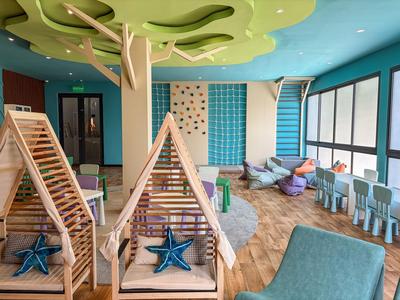 Moderner Hotelspielbereich mit Holzklettergerüsten, Sitzgelegenheiten und bunten Wanddekorationen.