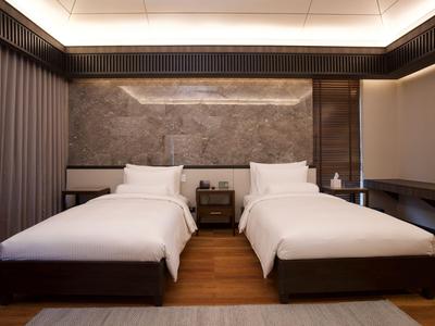 Modern eingerichtetes Hotelzimmer mit zwei Einzelbetten, grauem Kopfteil und Holzfußboden.