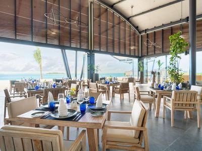 Offenes Restaurant mit Holzmöbeln und Blick auf den Strand und das Meer.