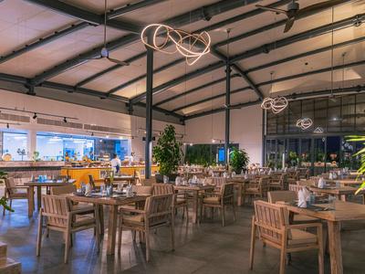 Großer Restaurantbereich mit Holztischen und Stühlen, moderner Beleuchtung und Pflanzen im Innenraum.