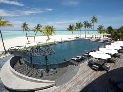 Hotelpool mit Sonnenliegen und Palmen am weißen Sandstrand unter blauem Himmel