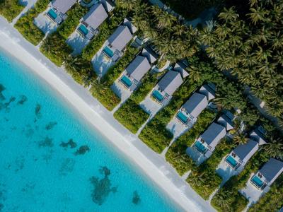 Reihe von Bungalows am Strand mit türkisfarbenem Wasser und dicht bewaldetem Hintergrund.