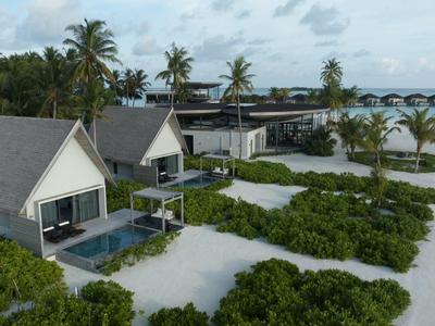 Luxuriöse Bungalows mit Pools am Strand, umgeben von Palmen und einem Steg im Hintergrund.