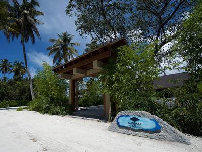 Eingang zu einem tropischen Hotel mit Sandboden, Palmen und grünem Laub unter blauem Himmel.
