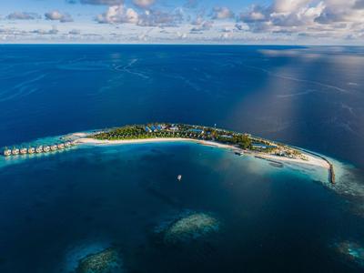 A narrow tropical island strip surrounded by clear blue water and clouds in the sky.