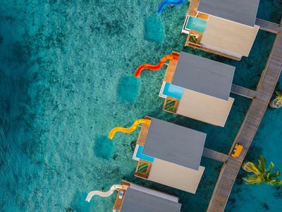 Aerial view of over-water bungalows with water slides and clear turquoise water.
