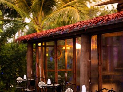 Hotel outdoor area with wooden floor, tables, and chairs under palm trees at sunset.