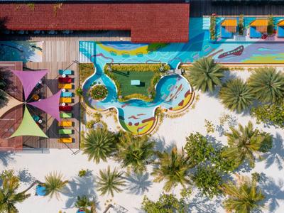 Aerial view of a resort with pools, sun umbrellas, and palm trees on a sandy beach.