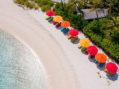 Beach with white sand, clear water, and colorful umbrellas along the shore.