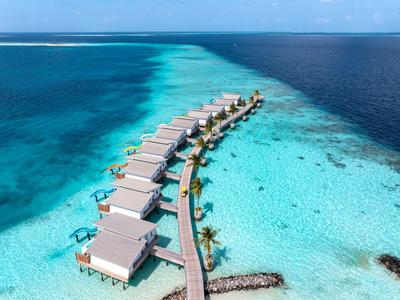 Row of overwater bungalows on stilts above clear turquoise water in a tropical setting.