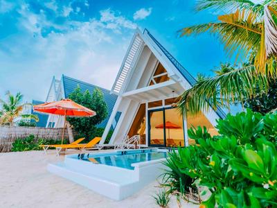 Modern A-frame house with pool and palm trees under a blue sky on a sandy beach.
