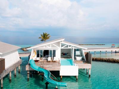 Overwater bungalows with waterslide overlooking the ocean under clear skies.