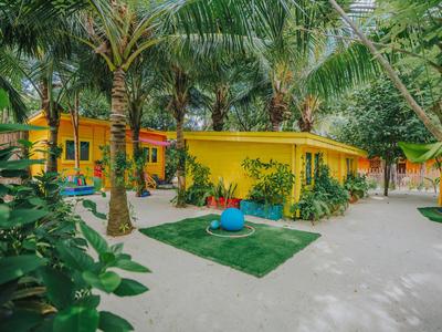 Yellow building in tropical garden with palm trees and sandy paths near beach.