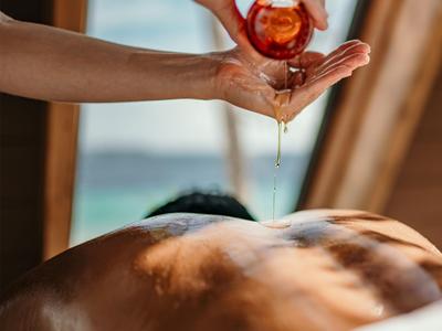 Someone pours massage oil onto the back of a relaxed person in a bright room with an outdoor view.